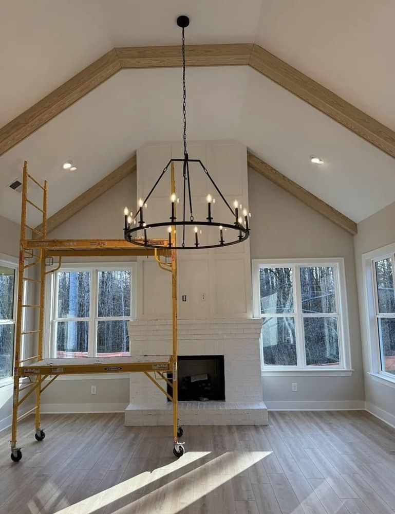 A modern living room with a fireplace, chandelier, and vaulted ceiling; construction scaffolding visible.
