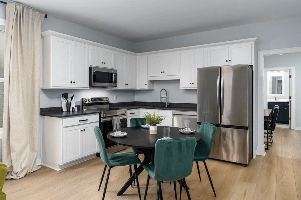 Modern kitchen with white cabinets, stainless steel appliances, and a round table with teal chairs.