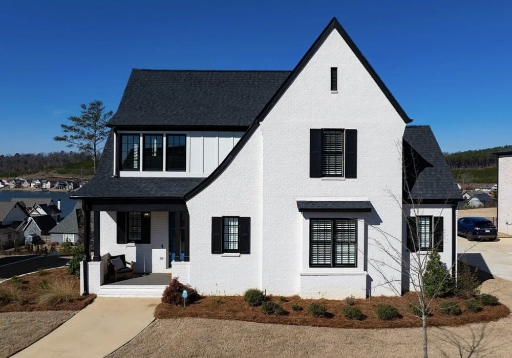 White house with black trim and shutters, a dark roof, and a small front porch on a sunny day.