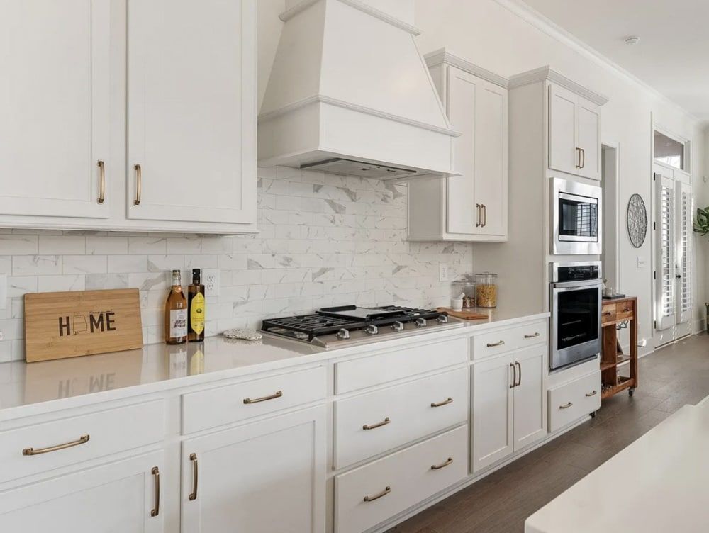 White kitchen with gas stovetop, range hood, and marble backsplash.