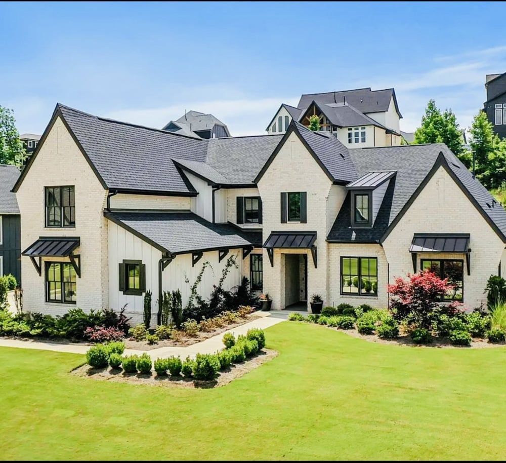 Two-story white brick house with black trim, awnings, and roof; set on green lawn.