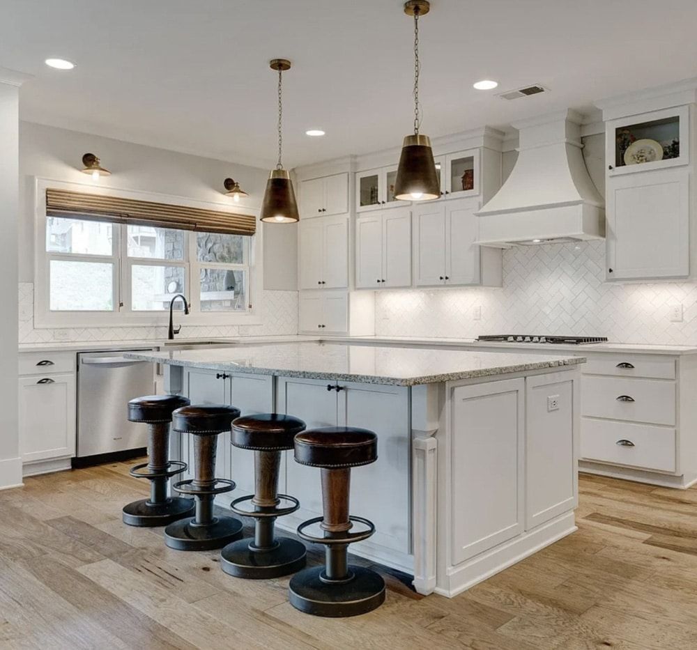 White kitchen with island, bar stools, pendant lights, and stainless steel appliances.
