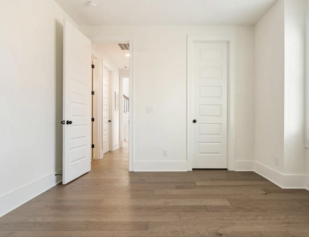 Empty white room with open doors, wood floor, and natural light.