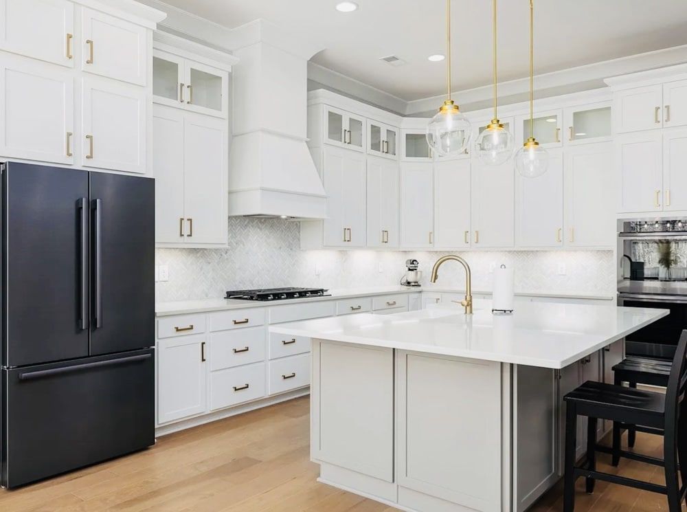 White kitchen with black fridge, island, cabinets, gold fixtures, and light wood floors.