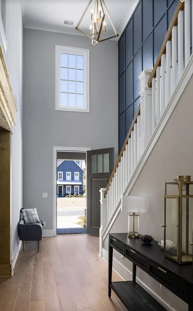 A bright foyer with open door, staircase, blue panel wall, and a decorative light fixture.