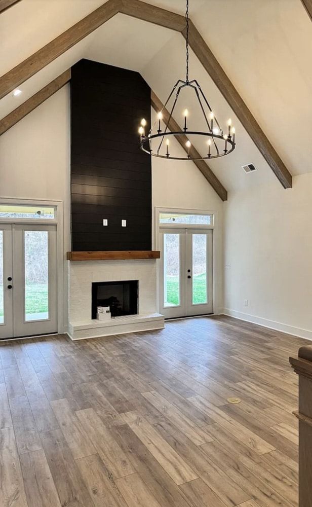 Living room with fireplace, cathedral ceiling, wood beams, chandelier, wood floors, and French doors.