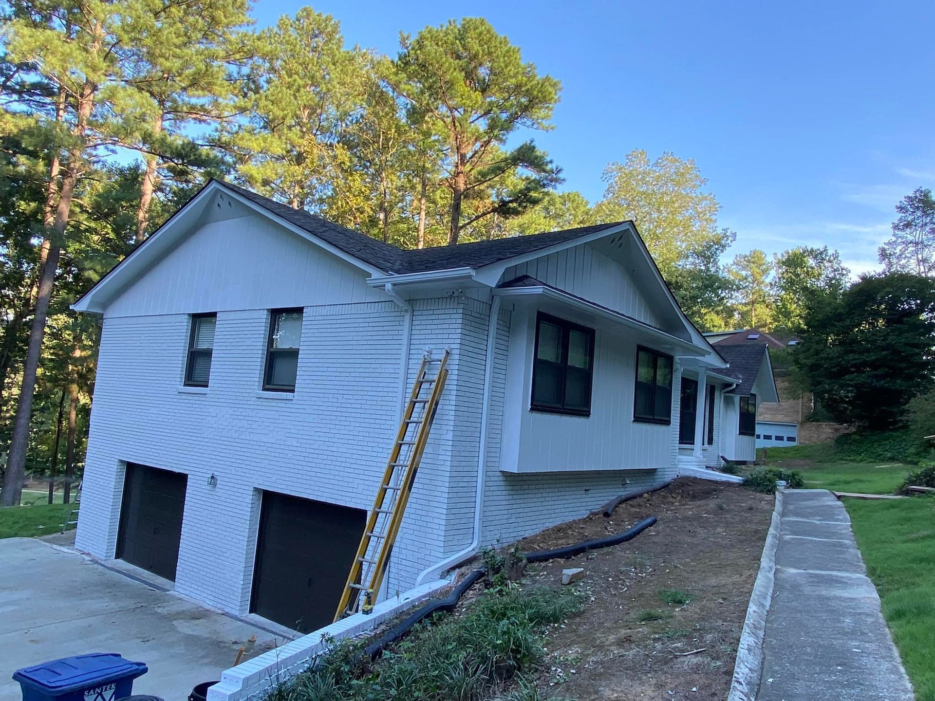 White house with black garage doors and windows, a ladder, and a concrete walkway.