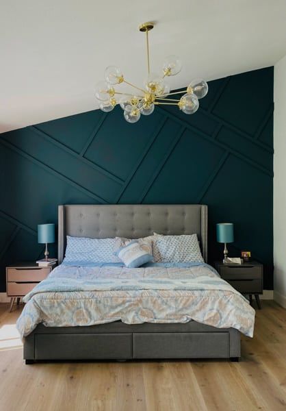 Bedroom with dark blue accent wall, gray bed, gold chandelier, and wooden floor.