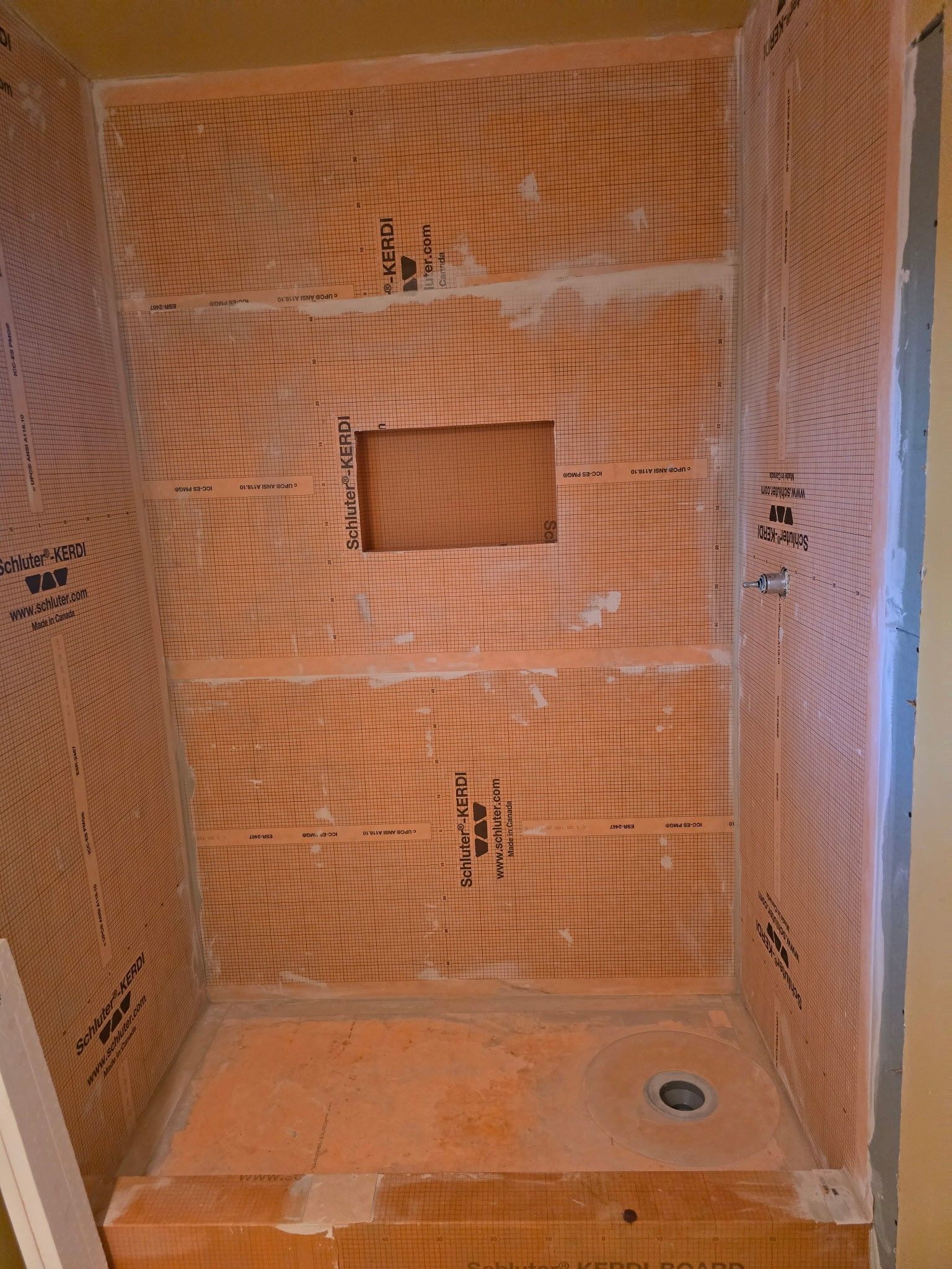 Orange-tiled shower stall under construction; walls and floor are covered with a mesh-like orange material.