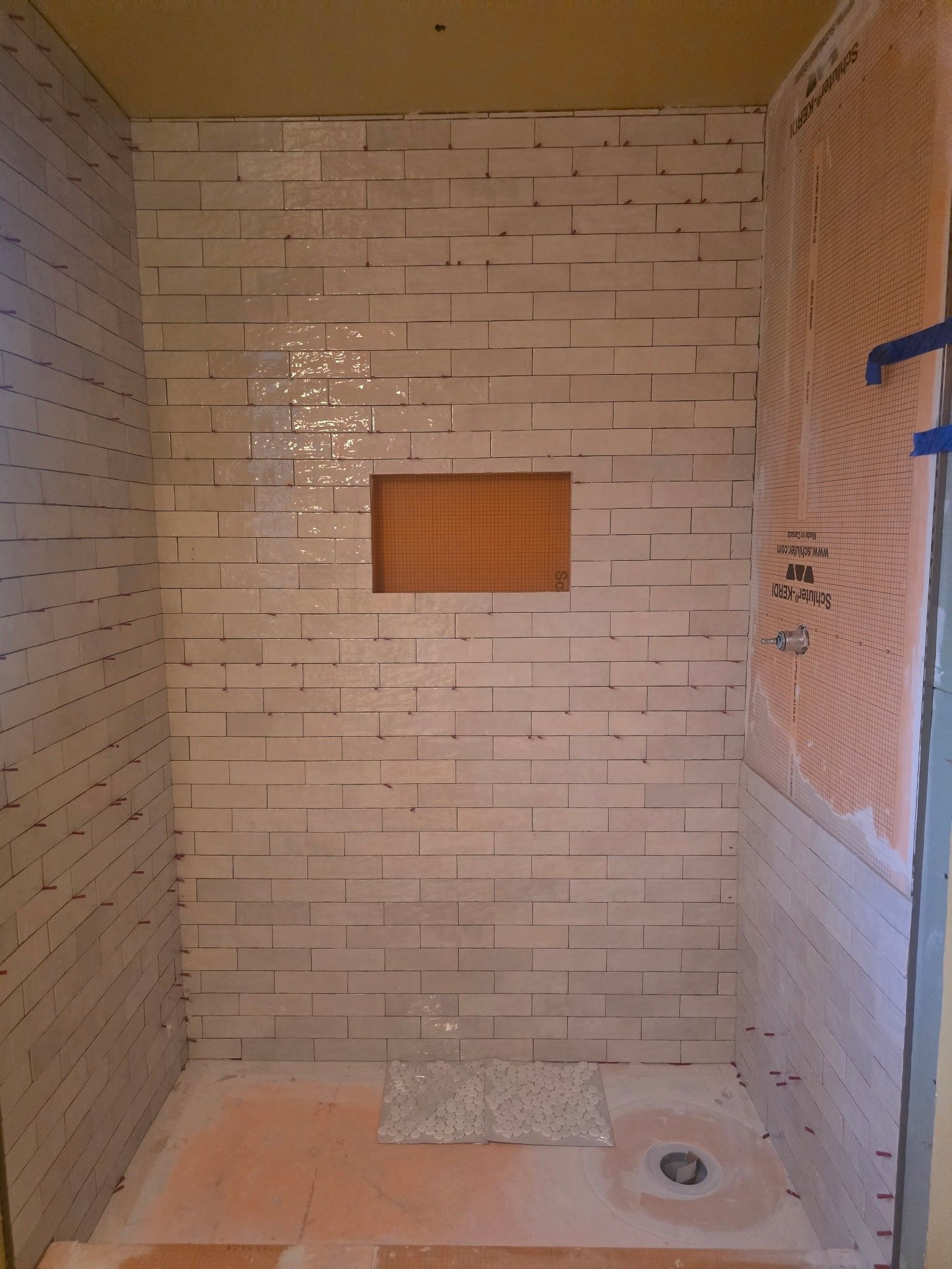 Shower stall with beige tile, orange waterproofing, and a built-in shelf.