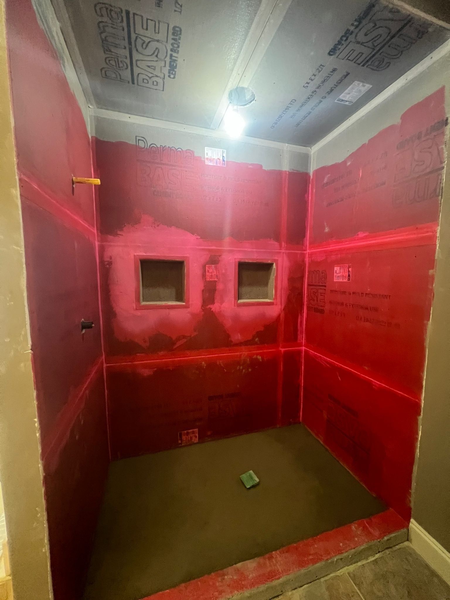 Red-walled shower stall under construction, with two recessed niches, laser level lines, and a sloped floor.