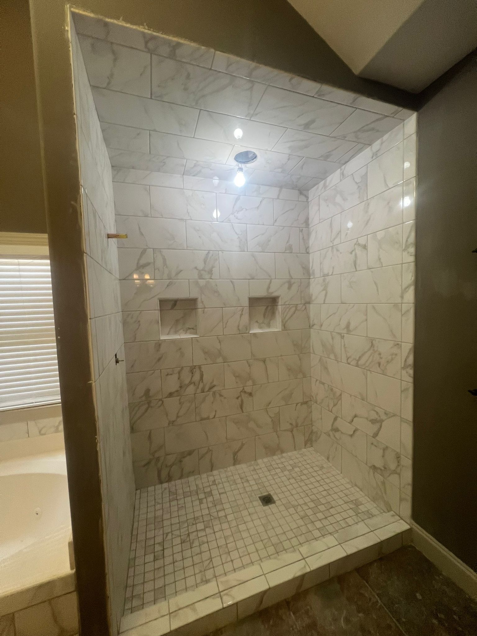 A tiled shower under construction, with marble-look walls and floor, and recessed storage.