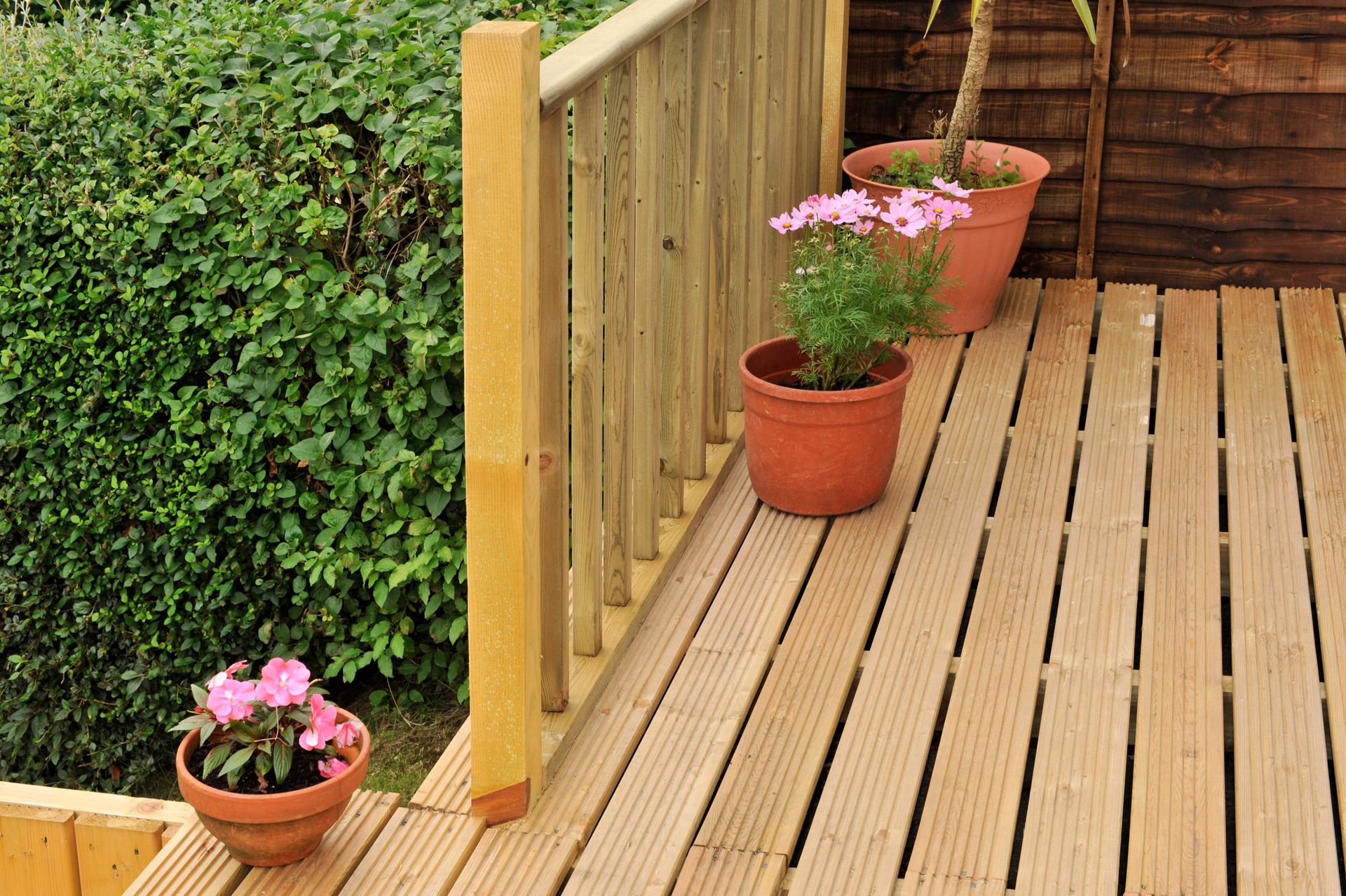 Wooden deck with railing, three flower pots, and lush greenery.