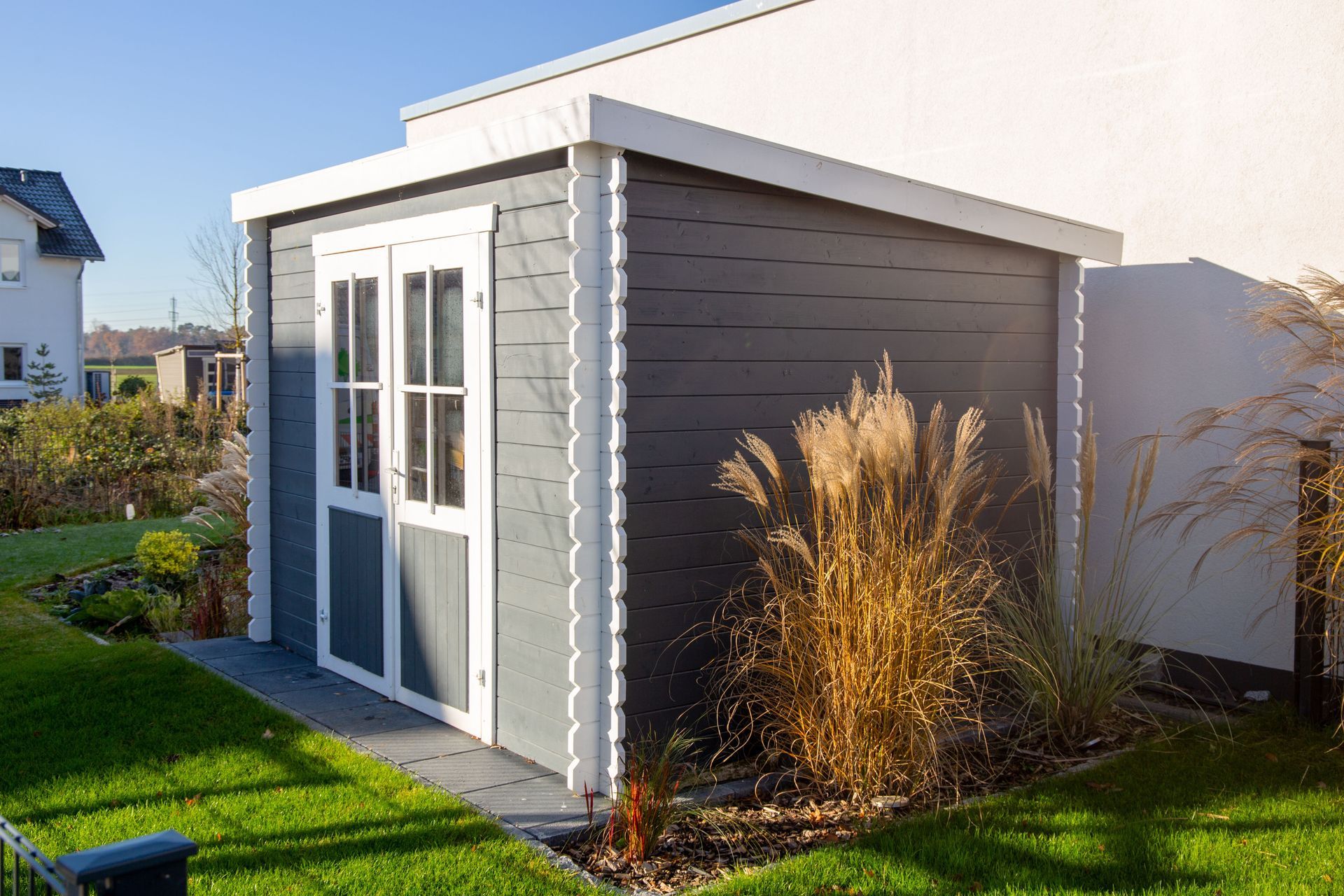 Gray and white shed with double doors in a yard with tall grass and sunlight.