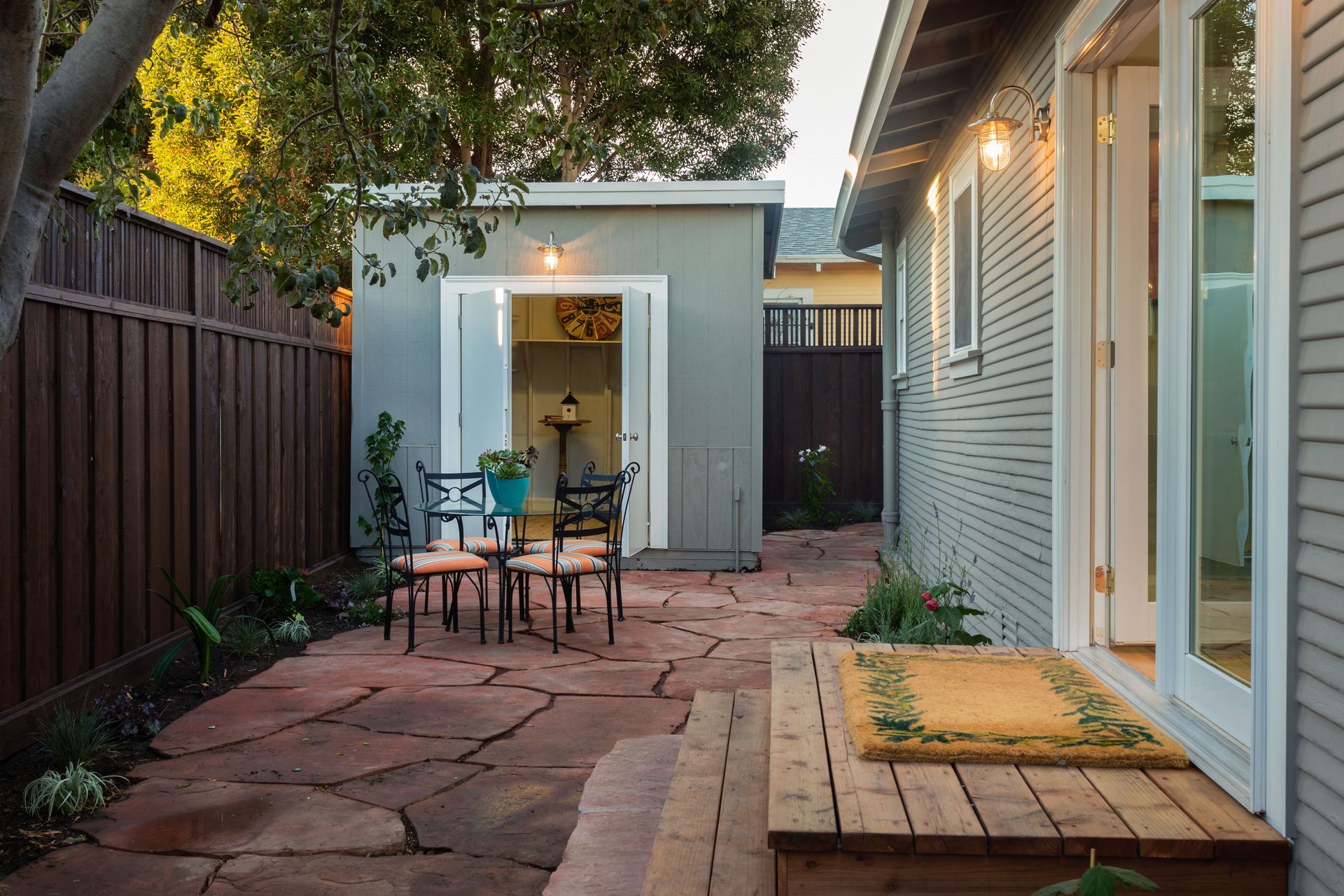 Patio with flagstone, chairs, shed, and house. Brown fence, gray shed, and blue walls.