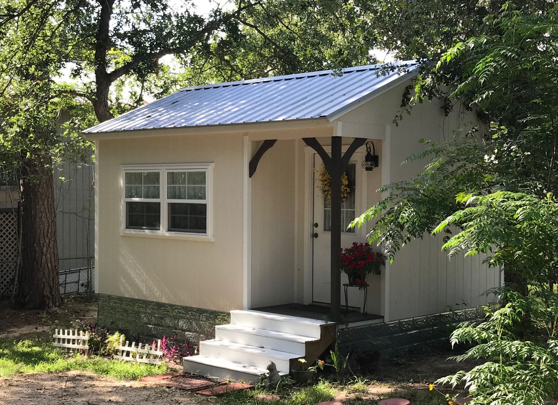 Small beige cabin with white trim, a metal roof, and steps leading to the entrance.