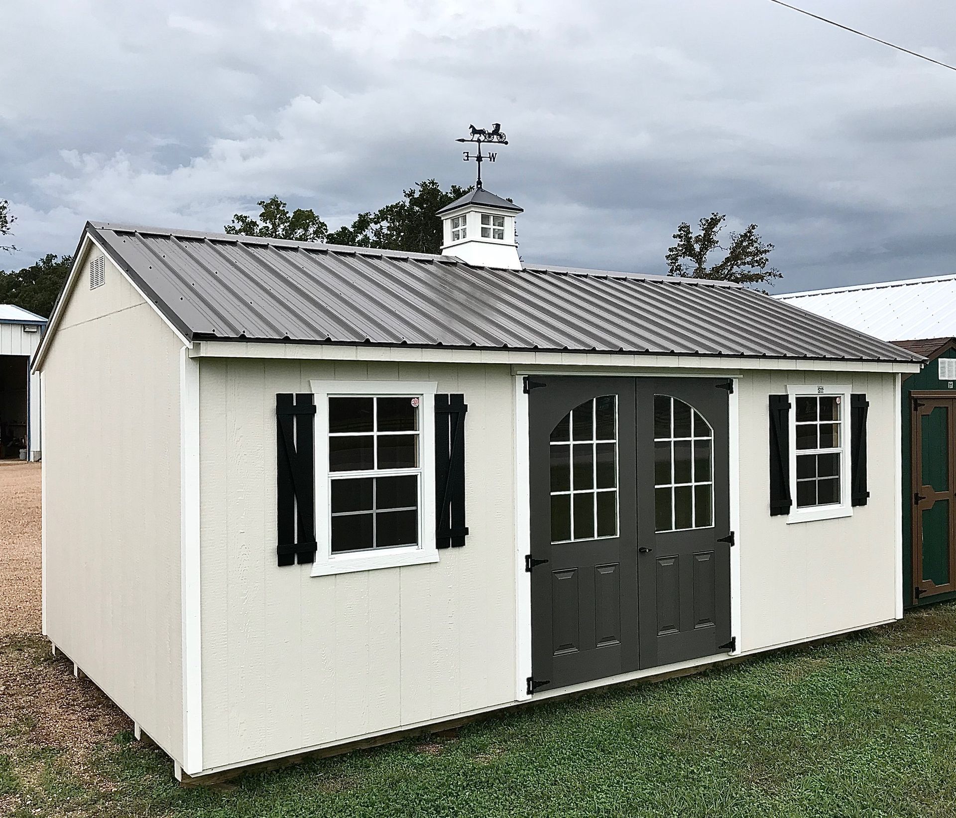 Tan shed with dark gray doors and shutters, metal roof, and cupola.
