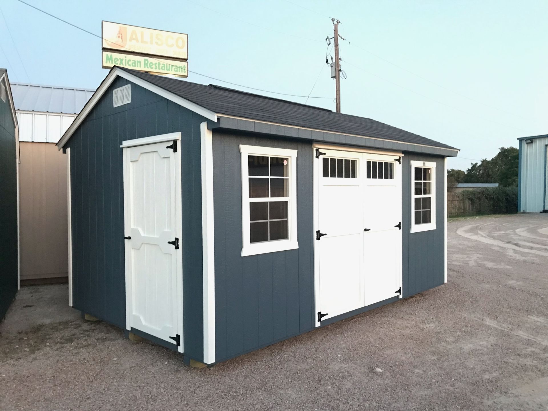 Blue storage shed with white doors and windows, gravel lot.