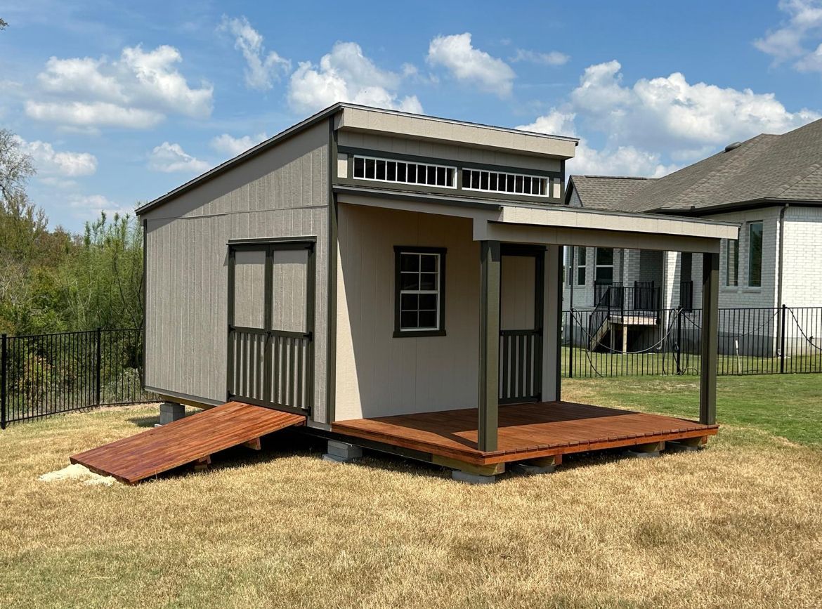 Gray barn with double doors, window, and a small cart on gravel in front of a wooden fence.