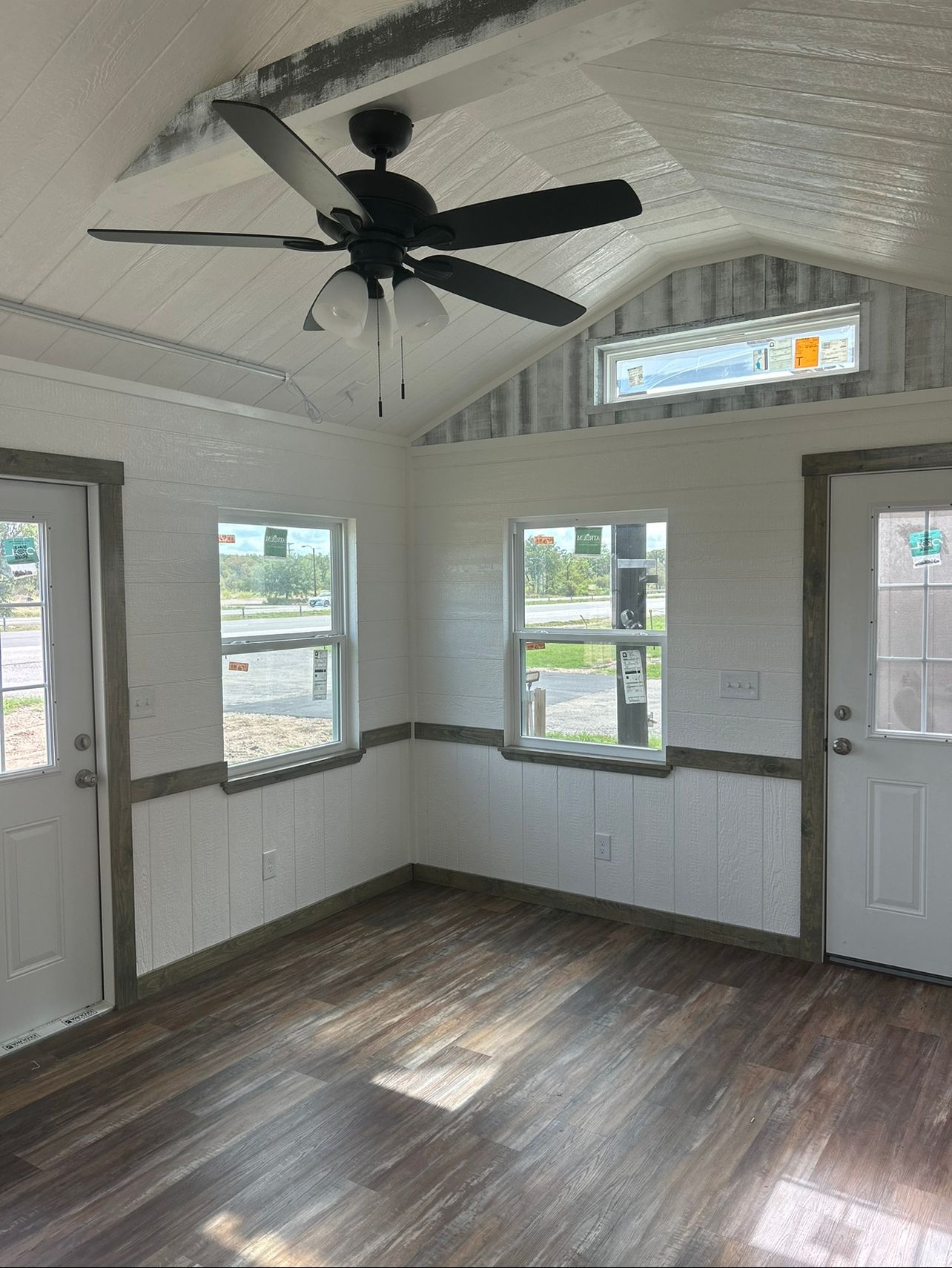 Interior of a small room with wood flooring, white walls, two doors, two windows, and a ceiling fan.