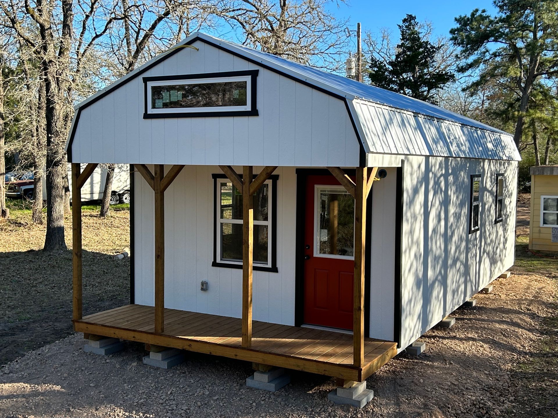 White tiny house with red door, small porch.