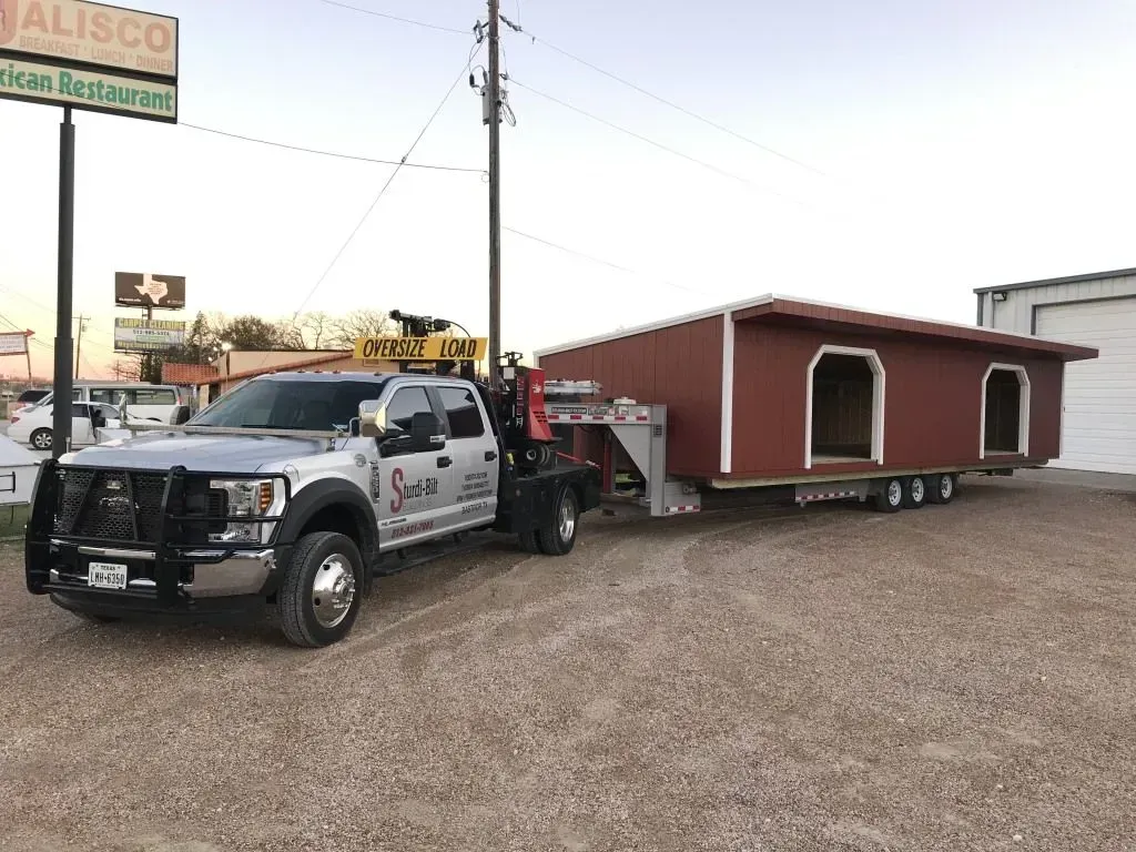 Silver truck towing a red shed on a trailer, parked in front of a restaurant.