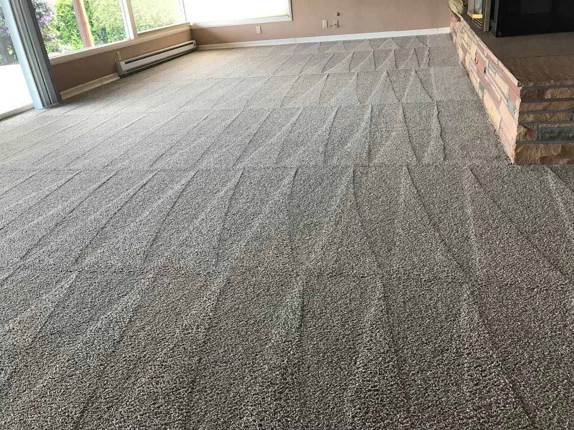 Gray speckled carpet in a room with windows and a brick accent wall.