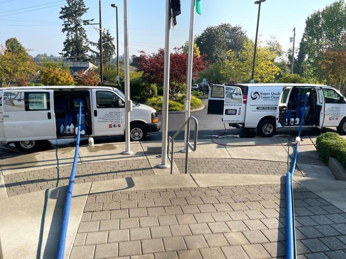 Two white vans with open doors parked near a building entrance. Blue railings and steps are in the foreground.