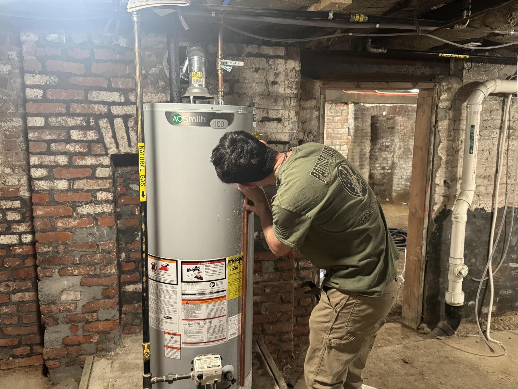 A man is working on a water heater in a basement.