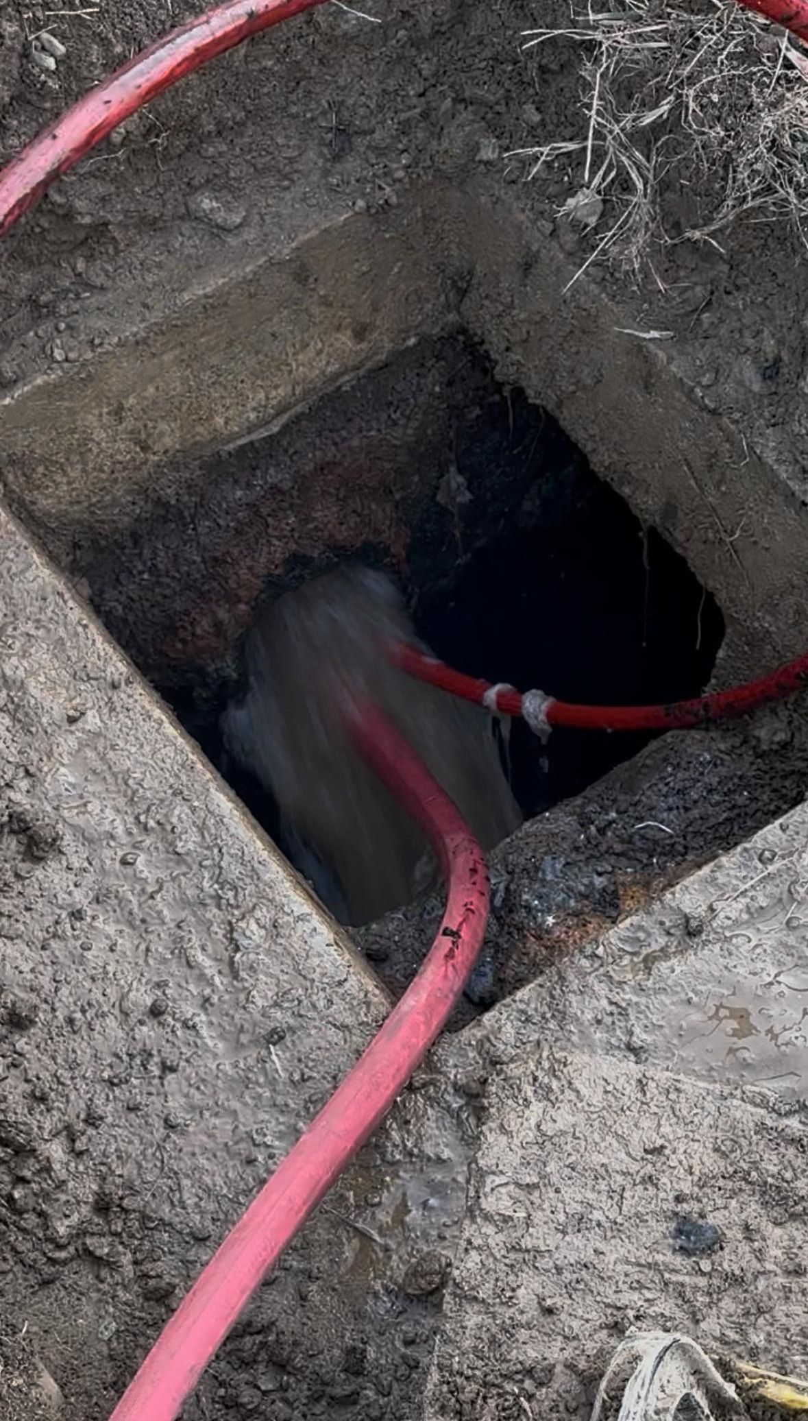 A red hose is coming out of a hole in the ground.