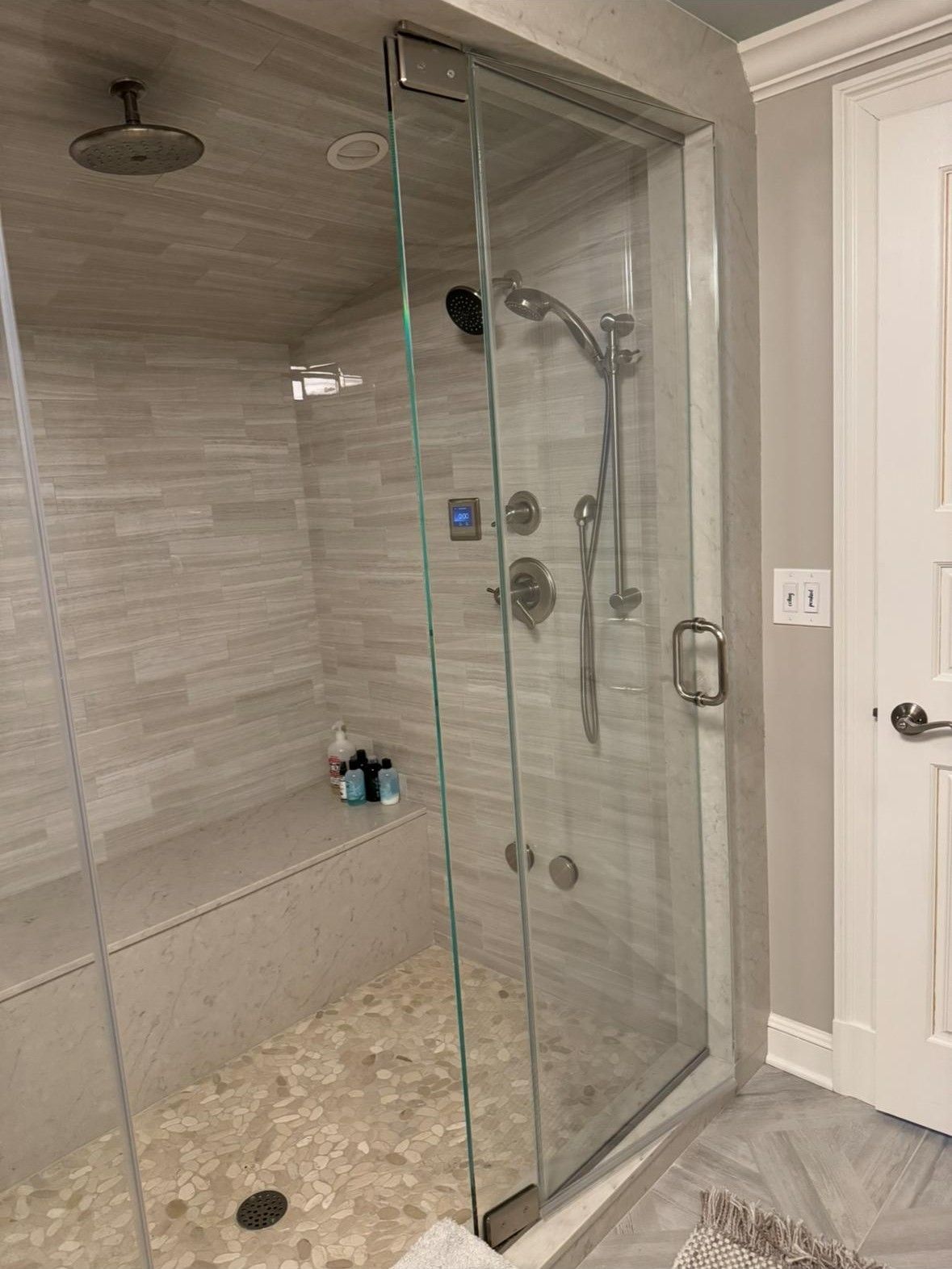 A bathroom with a walk in shower with a glass door and a bench.