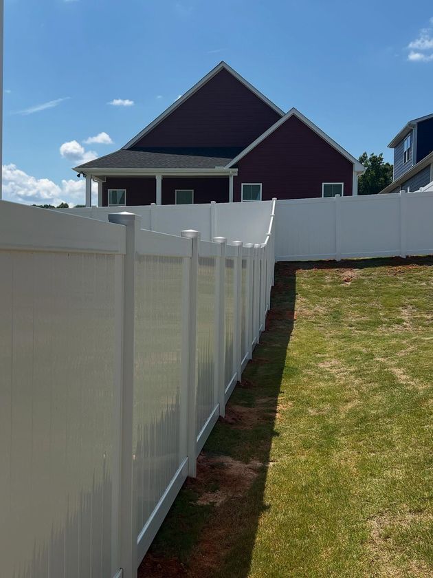 White vinyl fence beside a grassy yard, leading toward a dark house under a blue sky