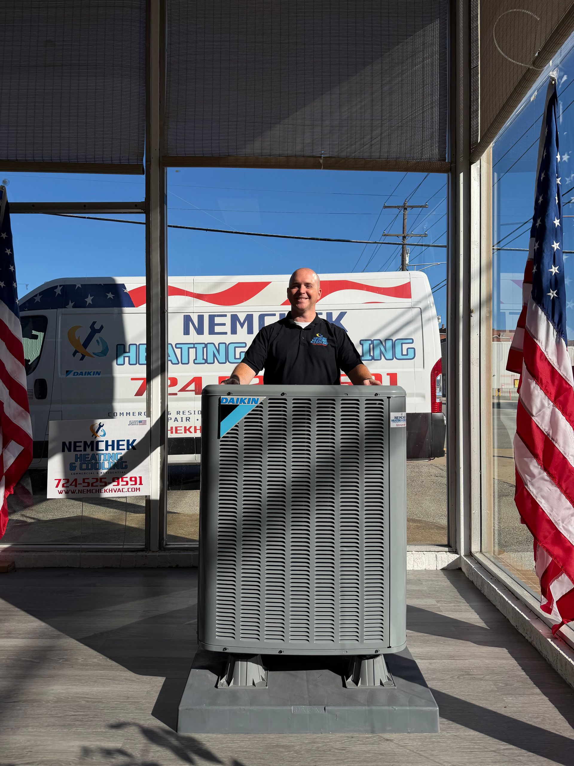 Person speaking at a podium on an outdoor stage with campaign banners and an American flag nearby
