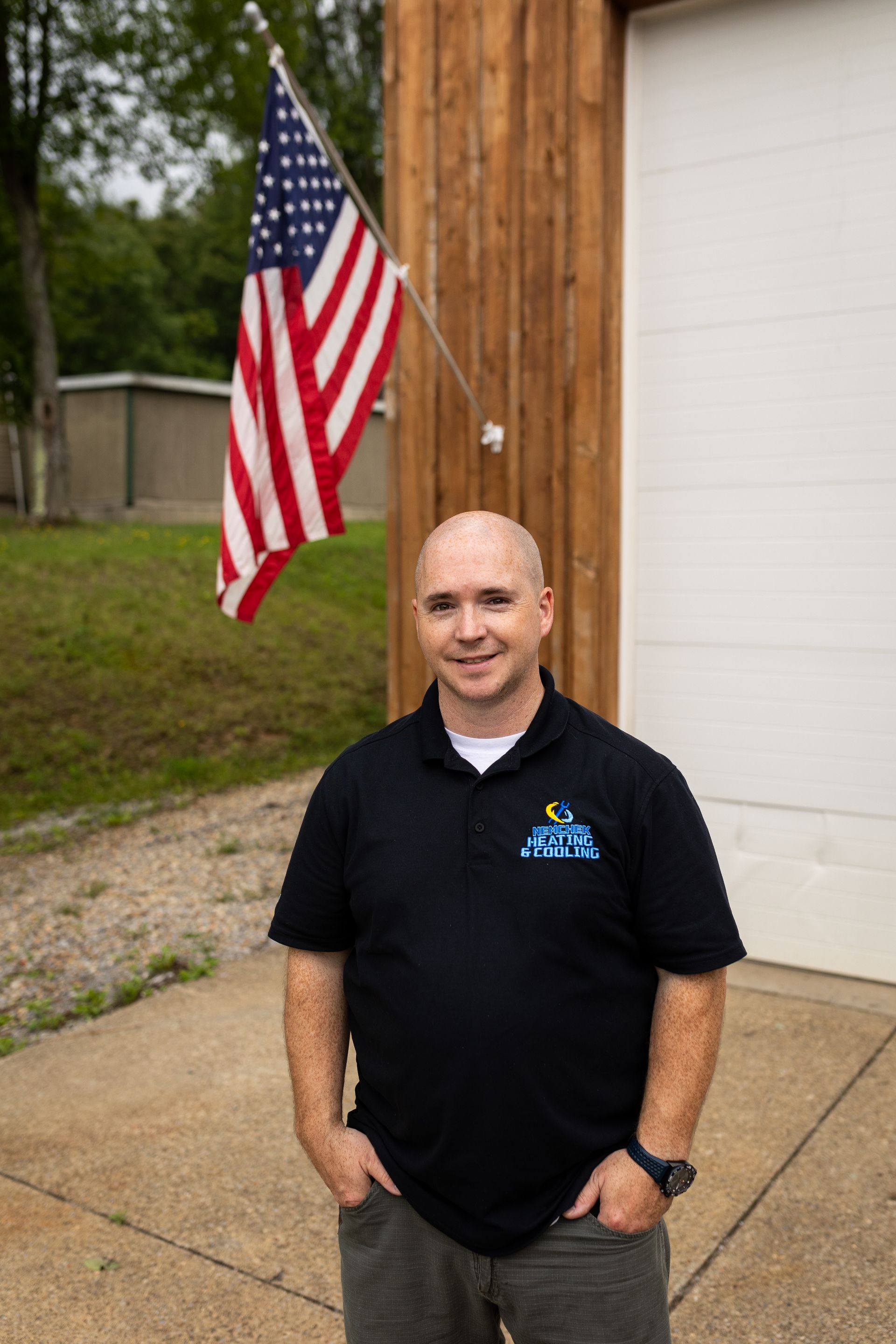 Rob standing by a wooden post with an American flag outside a building