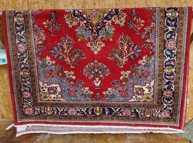 Red Persian rug with floral design, blue and gold border, hanging on a wooden surface.