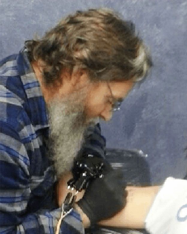 A man with a beard is getting a tattoo on someone 's arm