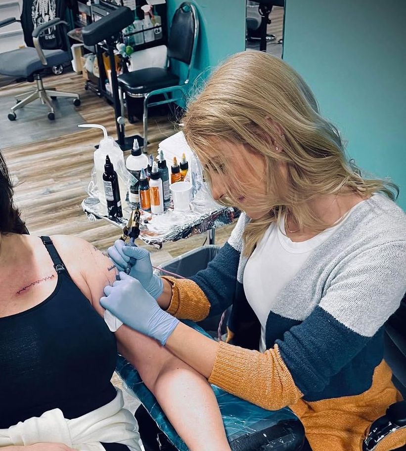 A woman is getting a tattoo on another woman 's back