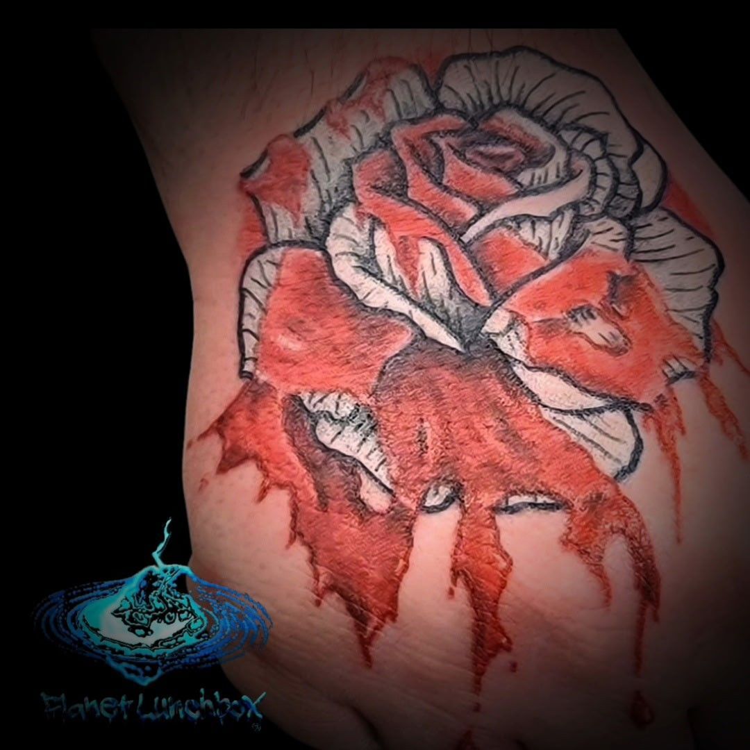 Red and white rose tattoo on skin, with bold black outlines and shaded petals.