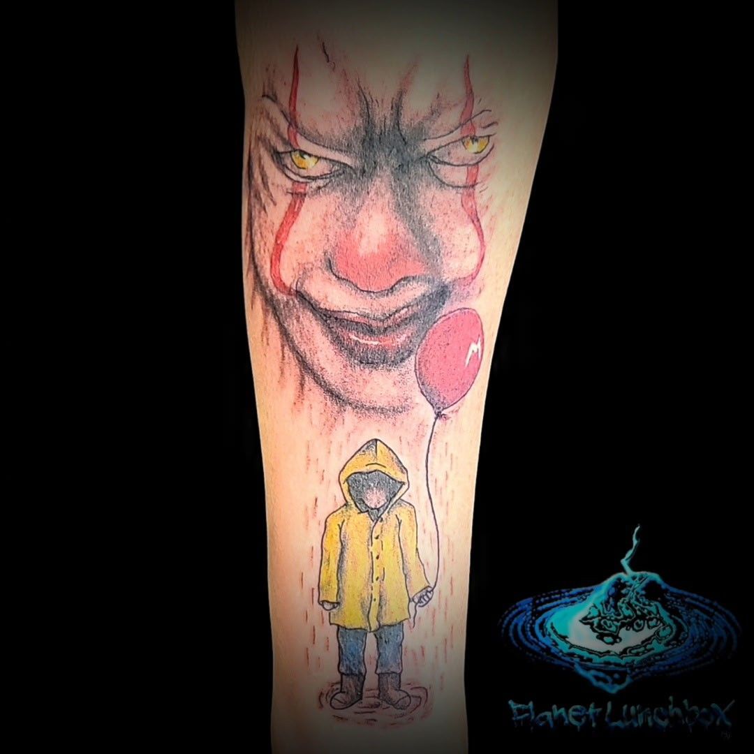 Creepy clown face tattoo above a child in a yellow raincoat holding a red balloon on a calf, with a glowing logo below