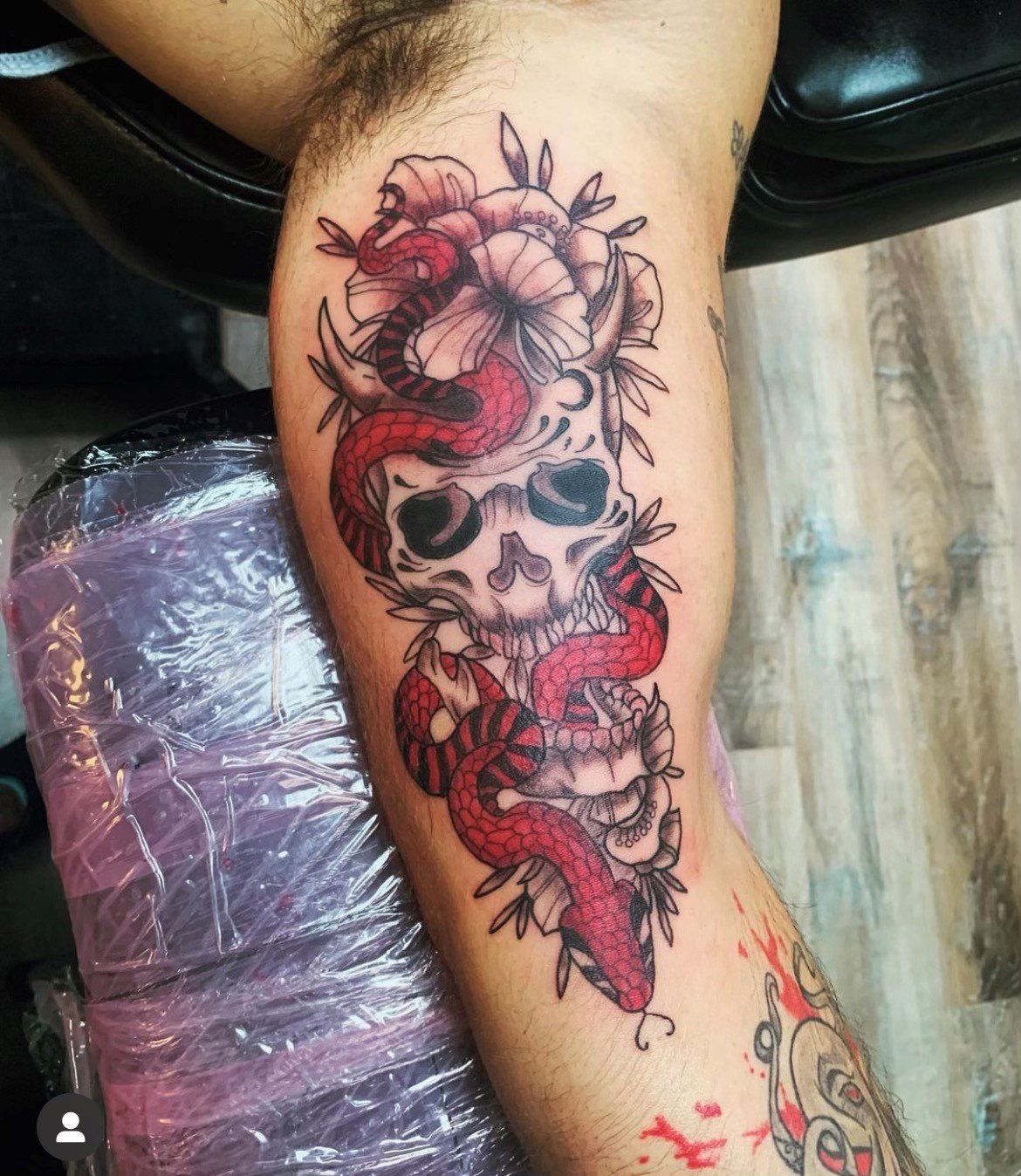 A person has a tattoo of a skull and a snake on their leg.