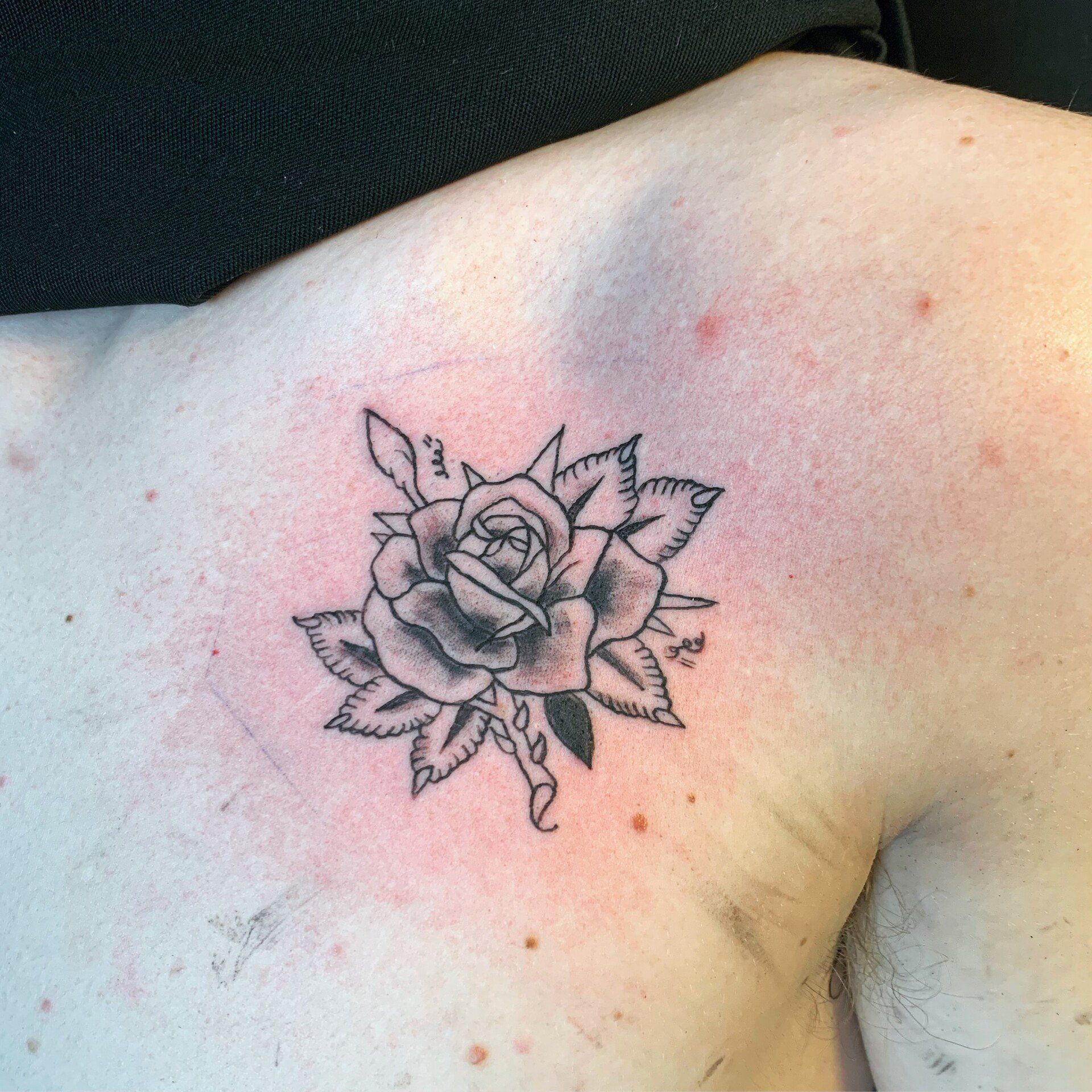 A black and white tattoo of a rose on a man 's shoulder