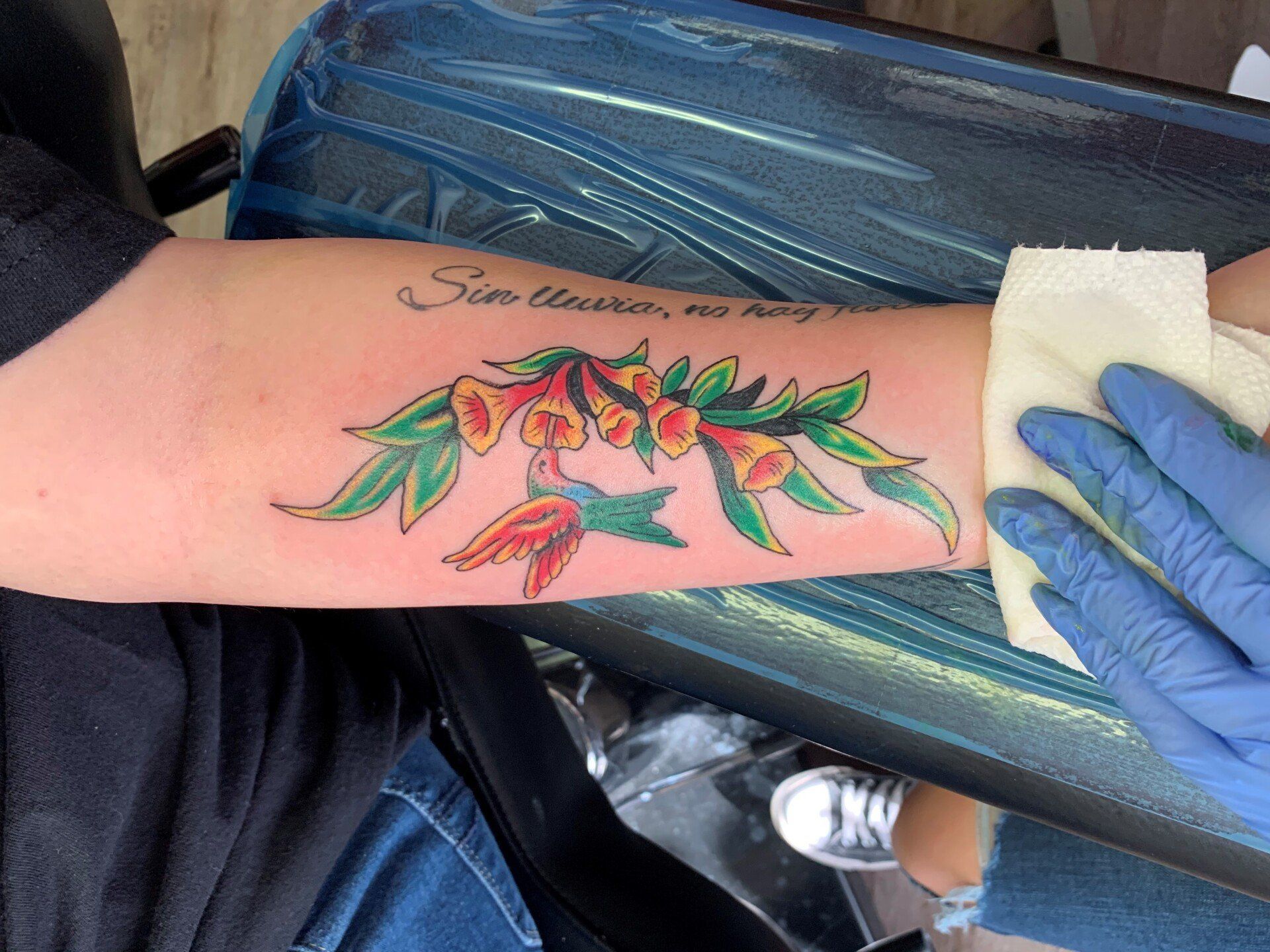 A person is getting a tattoo of a hummingbird and flowers on their arm.