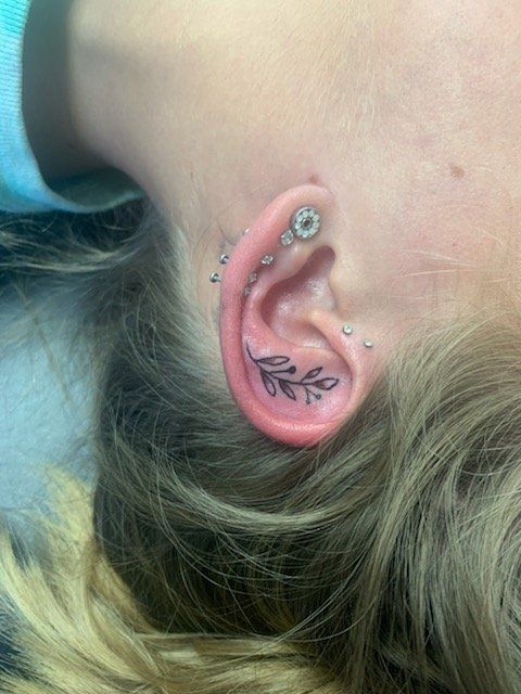 A woman has a tattoo of a leaf on her ear.