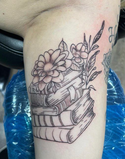 A tattoo of a stack of books with flowers on it