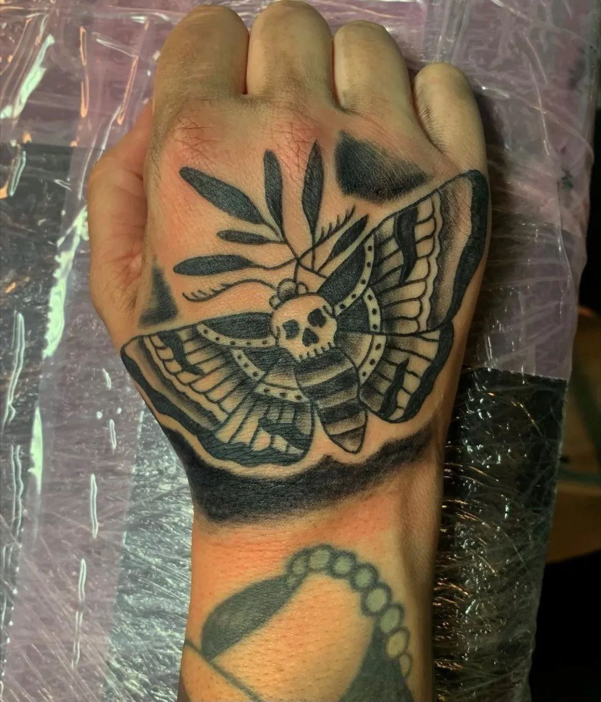 A hand with a tattoo of a moth with a skull on it