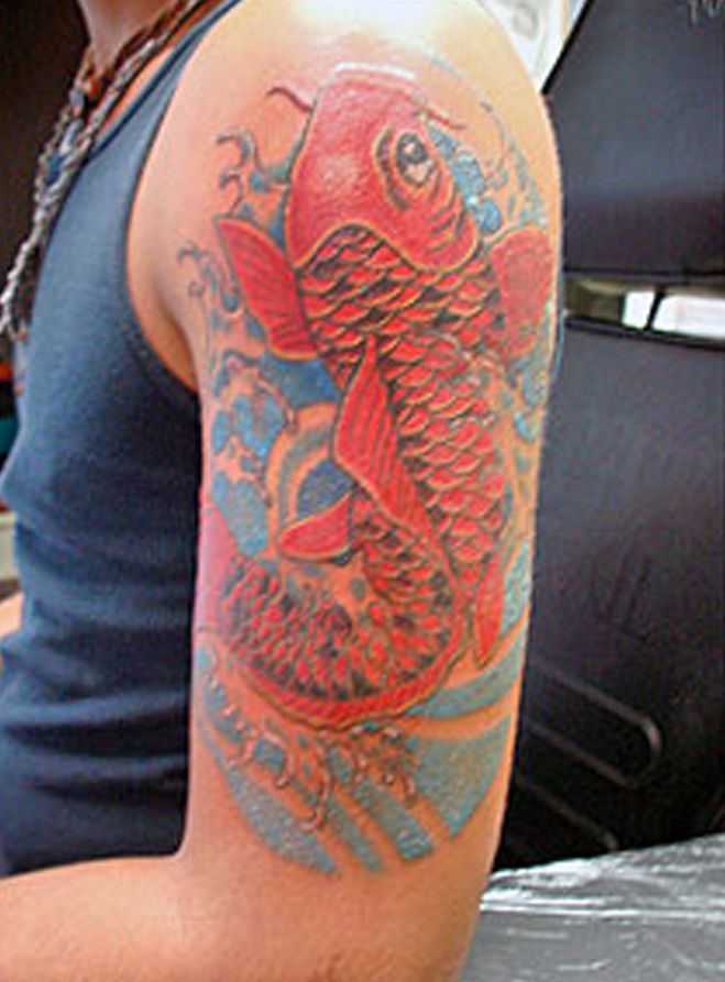A man has a tattoo of a red fish on his arm.