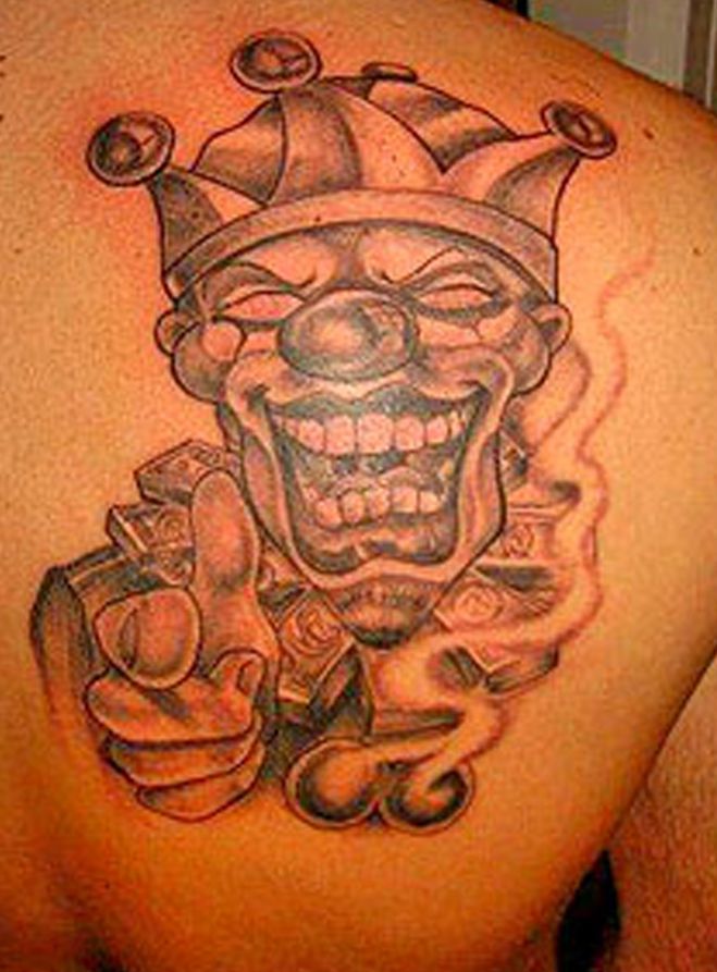 A black and white tattoo of a clown holding a pile of money on a man 's back.
