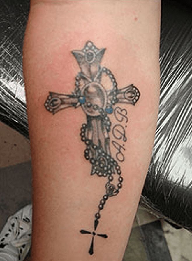 A person has a tattoo of a cross and rosary on their arm.