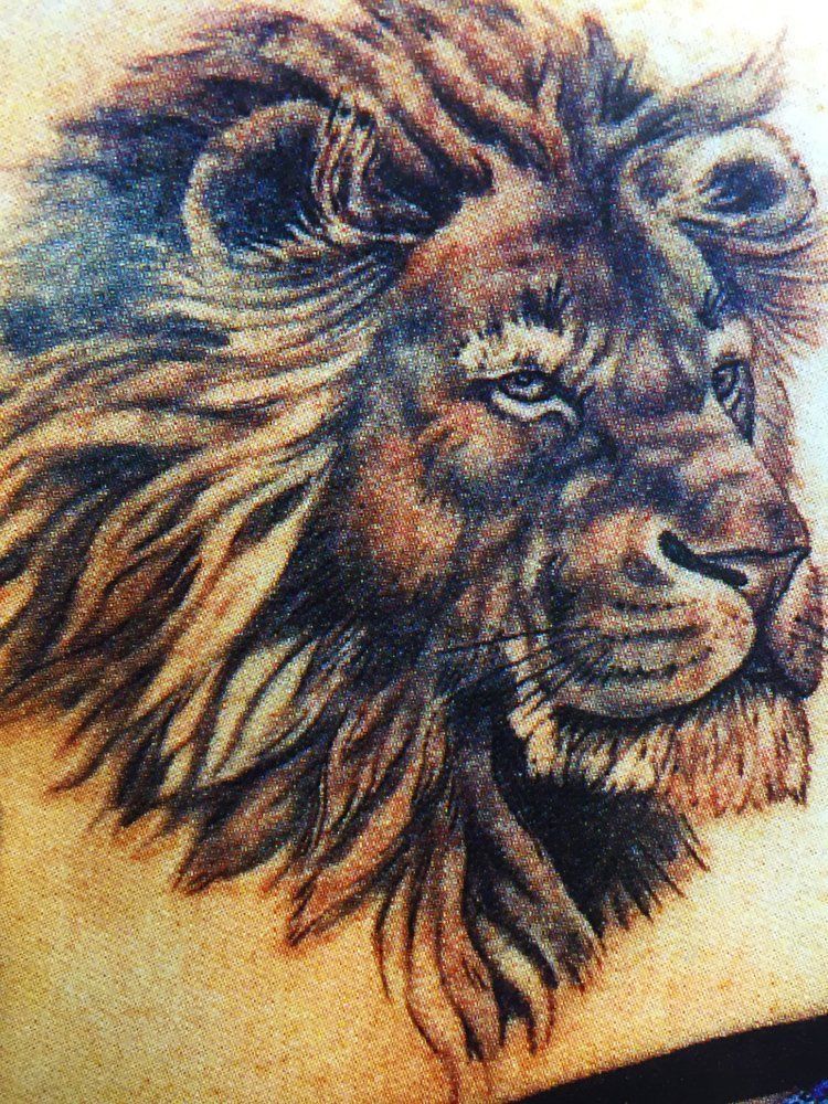A close up of a tattoo of a lion 's head on a person 's back.