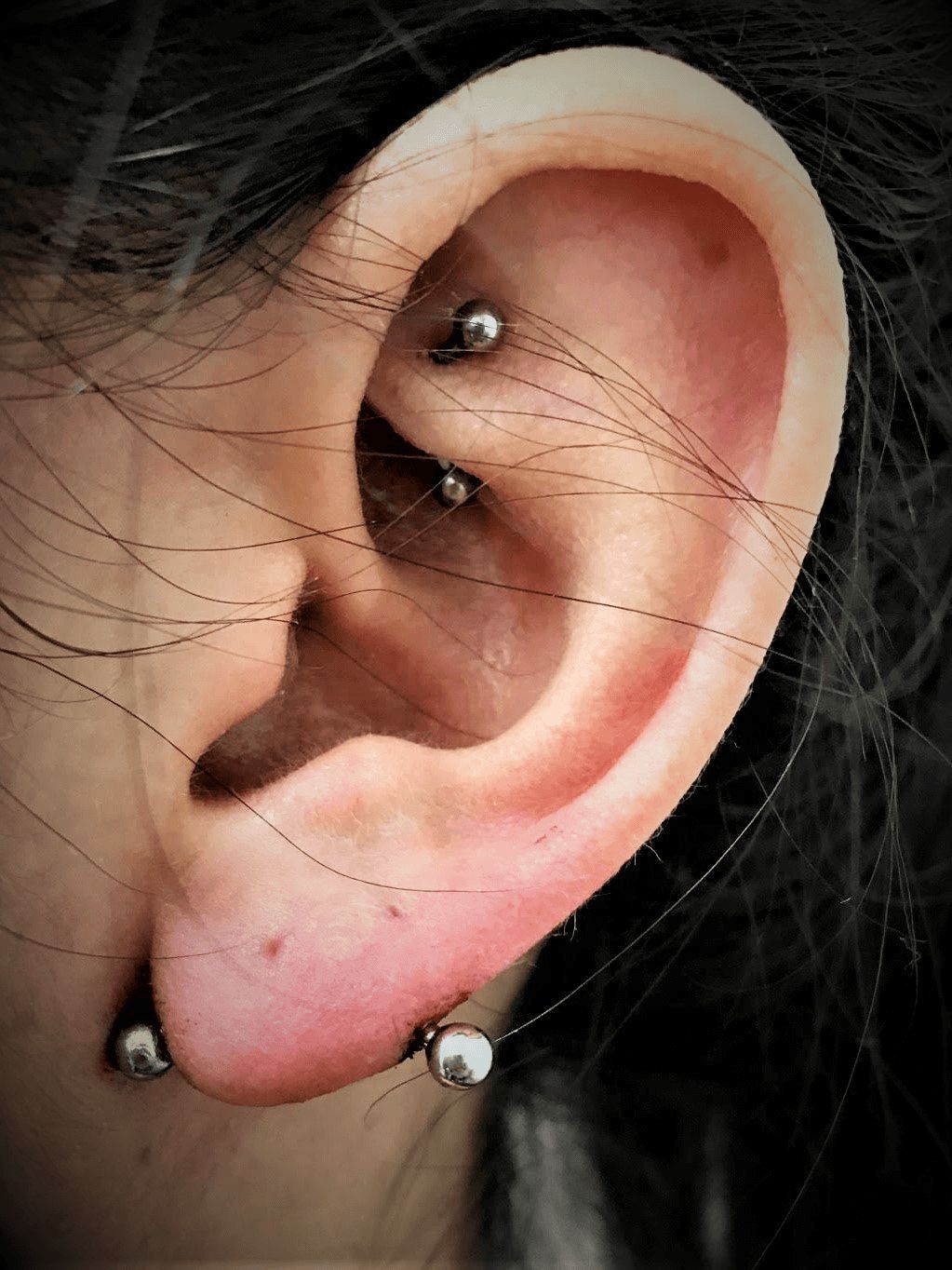 A close up of a person 's ear with multiple piercings